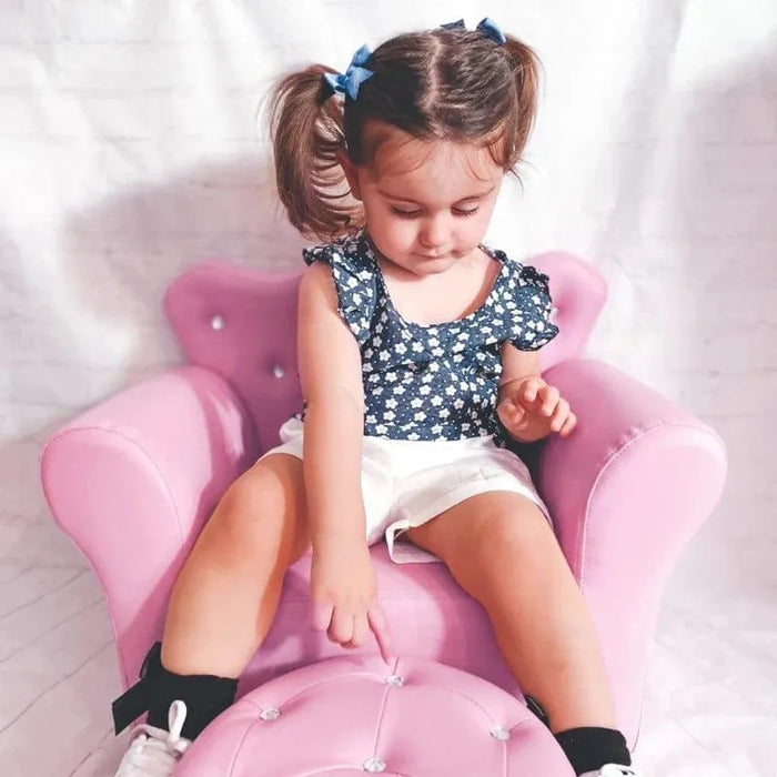 Toddler sitting on a pink kids armchair with crown backrest and crystal button details