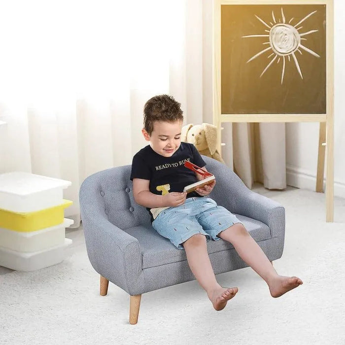 Child reading on grey kids armchair with wooden legs in bright playroom