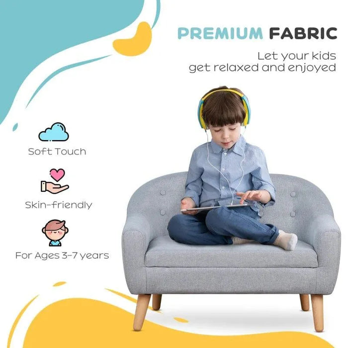 Child with headphones sitting on grey kids armchair sofa with wooden legs, using a tablet