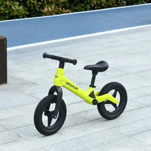 Green and black kids balance bike with adjustable seat and handlebar on pavement