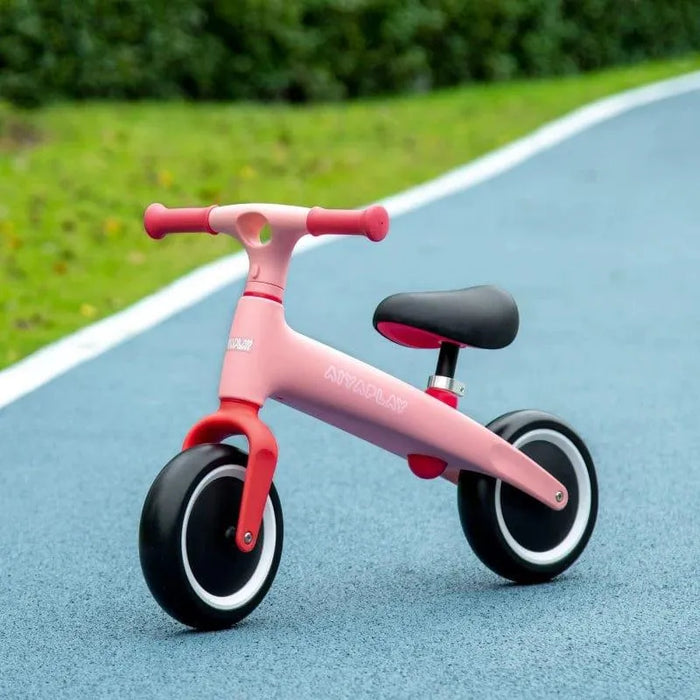Pink kids' balance bike with adjustable seat and EVA tires on outdoor blue path