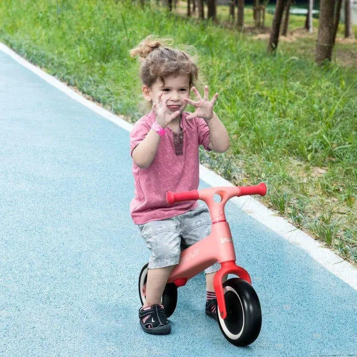 Child riding pink kids balance bike with EVA tyres on blue outdoor path