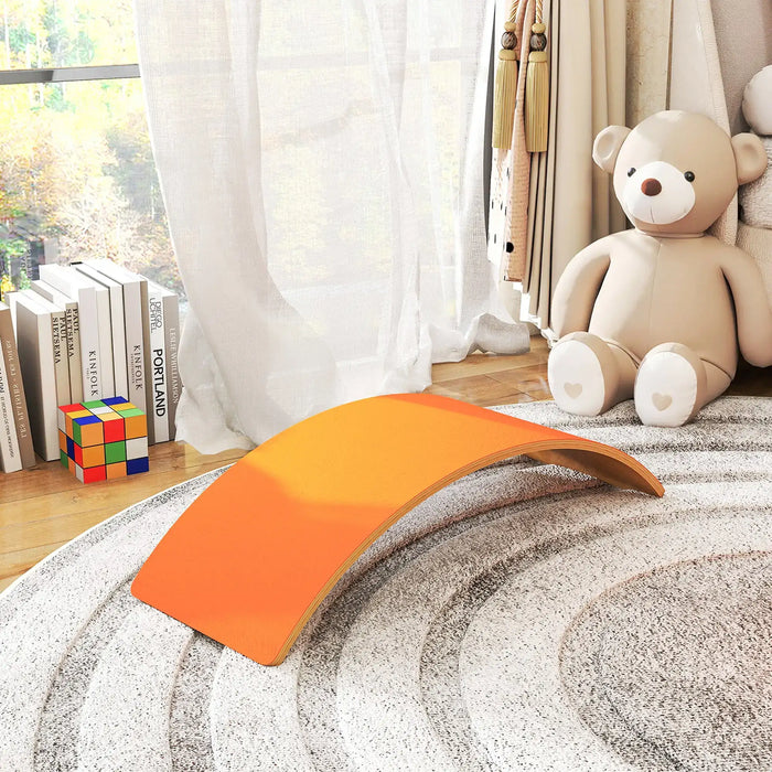 Orange wave-shaped object on a textured surface with a teddy bear and books in the background.