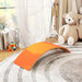 Orange wave-shaped object on a textured surface with a teddy bear and books in the background.