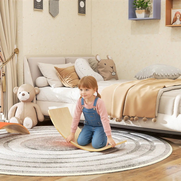 Child playing on a wooden balance board in a cozy bedroom with a bed and teddy bear in the background.