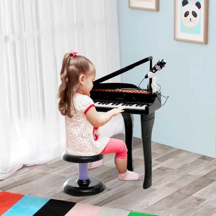 Young girl plays kids black 37-key mini grand piano with stool and microphone in playroom.