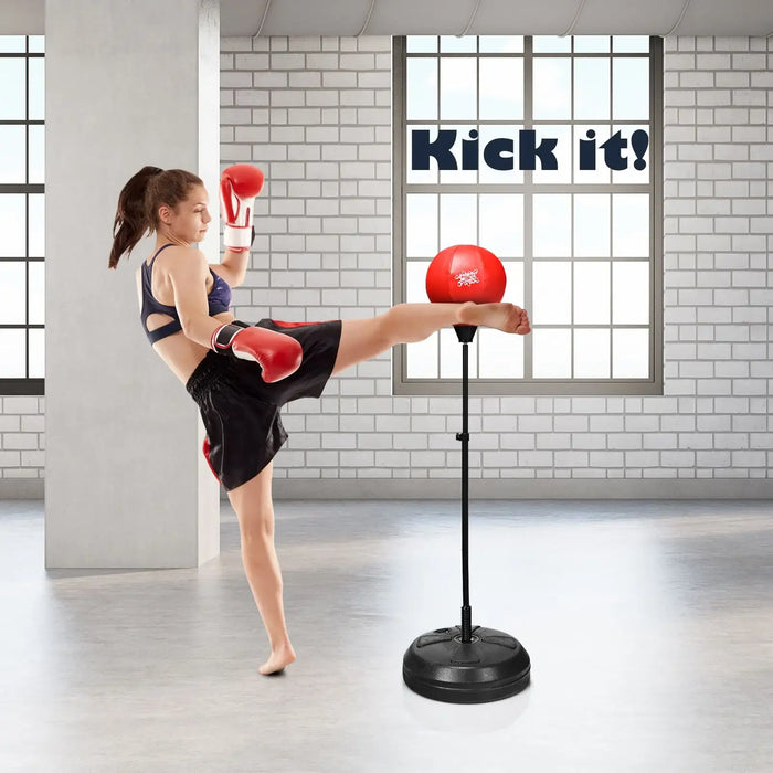 Woman in boxing gloves and shorts kicking a red punching bag in a bright gym with large windows