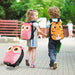 Two kids holding hands wearing cute owl and tiger animal backpacks with matching owl rolling suitcase outdoors