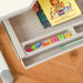Close-up of kids' grey adjustable desk tray with colored letters, pencil, and children's book.