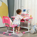 Toddler at pink adjustable kids desk and chair set with USB lamp, reading a book indoors.