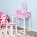 Pink kids dressing table set with mirror and stool, featuring cartoon accents, next to a stuffed pink elephant.