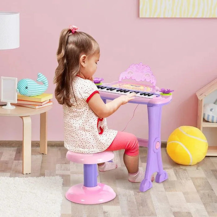 Little girl playing pink kids electronic keyboard with microphone in a playroom