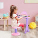 Little girl playing pink kids electronic keyboard with microphone in a playroom