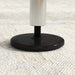 Close-up of adjustable steel gym bar base with black round foot on textured beige surface