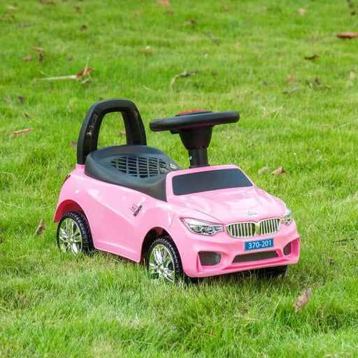 Pink kids ride-on car with steering wheel and black seat on green grass