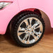 Close-up of chrome wheel on pink kids ride-on car on wooden floor