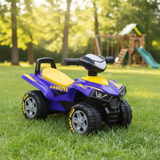 Purple and yellow Goodyear kids ride-on ATV toy on grass with playground in background