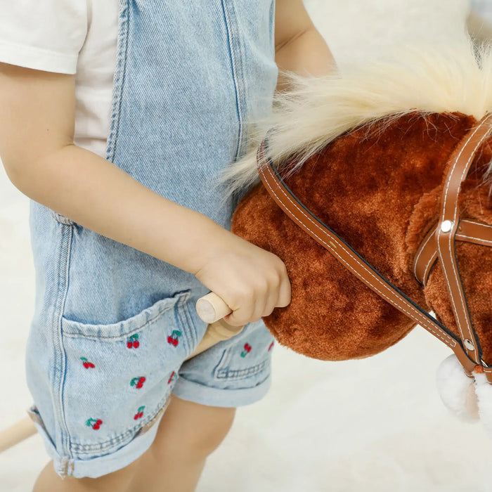 Child holding a toy horse with a soft brown body and leather reins.