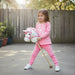 Child in pink outfit holding a toy horse in a backyard setting