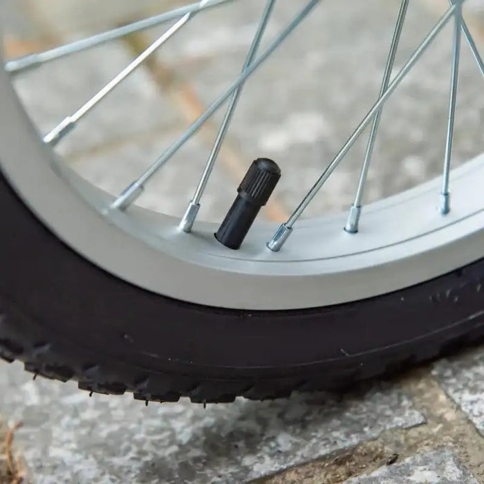 Close-up of a kids scooter wheel with tire valve and silver spokes on pavement