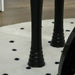 Black piano legs on white rug with black polka dots, close-up view