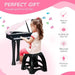 Young girl playing black kids mini grand piano keyboard with LED lights, seated on a matching black stool, with features including easy to clean, suitable for kids ages 3-6, and premium sound highlighted on a pink background.