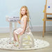 Girl sitting at white kids mini grand piano keyboard on round play mat in a playroom