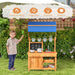 Child playing with fir wood outdoor play kitchen with blue adjustable canopy and toy cooking set
