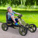 Smiling child riding green and black kids pedal go kart with handbrake on outdoor path