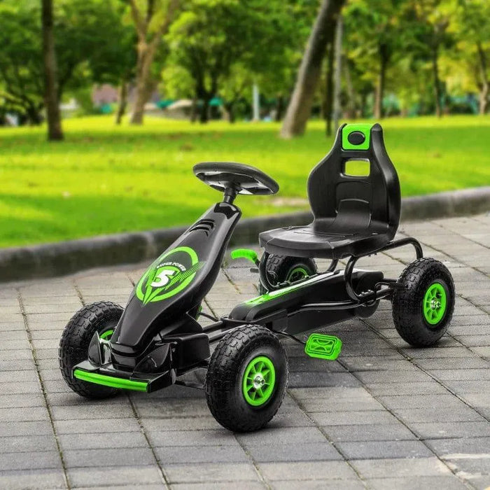 Green and black kids pedal go kart with shock-absorbing suspension on paved path outdoors