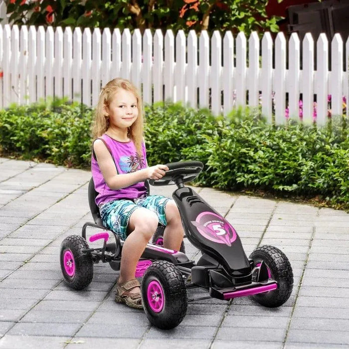 Child riding pink and black kids pedal go kart on paved path with white picket fence