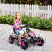 Child riding pink and black kids pedal go kart on paved path with white picket fence