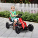 Smiling boy riding red and black kids pedal go kart on outdoor path near white fence