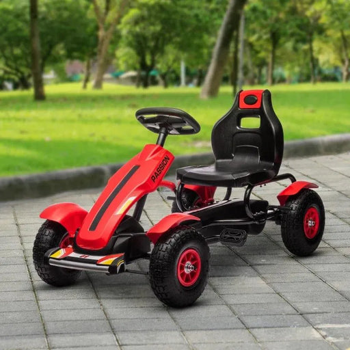 Red kids pedal go kart with rubber wheels and suspension on a paved path in a park