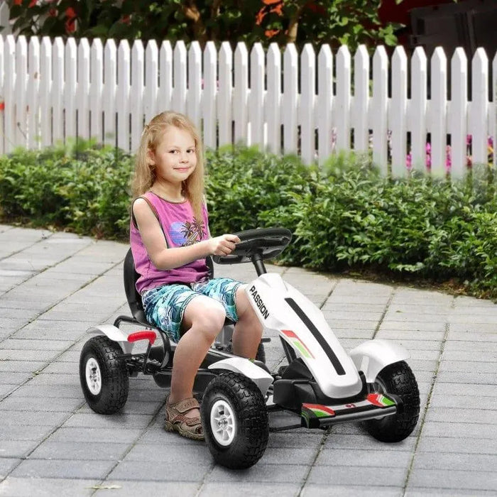 Child riding white and black kids pedal go-kart with handbrake outdoors on pavement