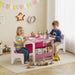 Two kids playing at pink and white children table with wooden blocks, books, and toys in bright playroom