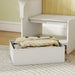 White storage ottoman with folded blanket underneath a wooden table.