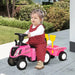 Toddler riding pink kids tractor ride-on toy with trailer outdoors