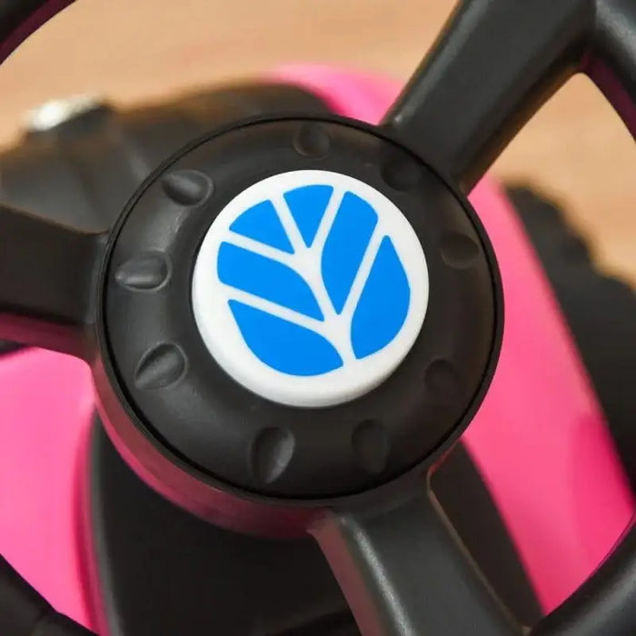 Close-up of a black steering wheel with blue logo on pink kids' ride-on tractor