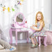 Smiling girl at pink kids vanity table with mirror, stool, drawer, and play makeup in bright room