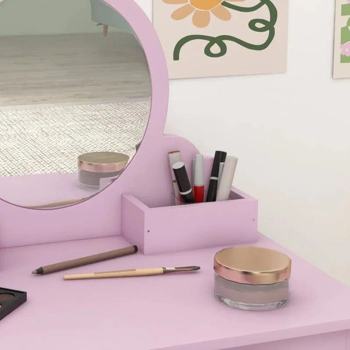 Pink kids vanity table set with mirror, makeup brushes, pens, and art on the wall