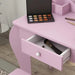 Pink kids vanity table with open drawer, makeup palette, brush, and wooden floor
