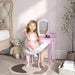 Young girl at pink kids vanity table set with mirror in bedroom, teddy bear nearby