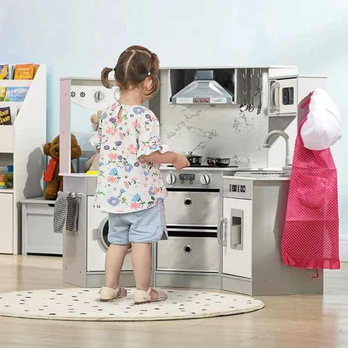 Child playing at grey and white wooden kitchen playset with chef costume and accessories