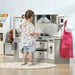 Child playing at grey and white wooden kitchen playset with chef costume and accessories