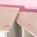 Light wood tabletop detail from kids wooden kitchen playset against pink wall
