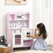 Girl playing with pink wooden kids kitchen playset featuring toy clock, sink, and storage