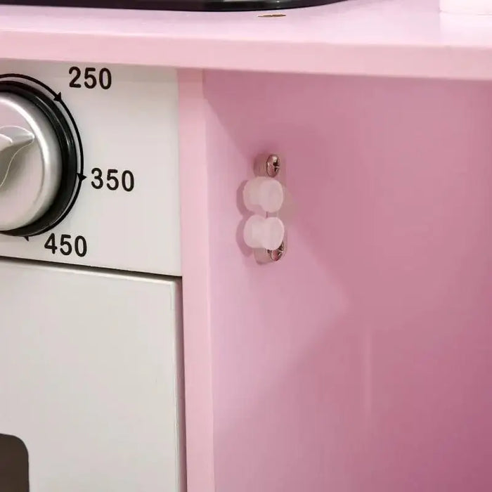 Close-up of pink and white kids' wooden kitchen playset with oven knob and details.