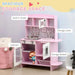 Pink wooden kids kitchen playset with storage, toy clock, sink, cabinets, and built-in hooks.