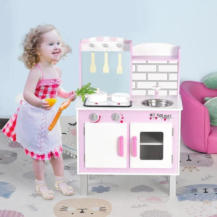 Child playing with pink wooden kids kitchen playset with pots, pans, and utensils